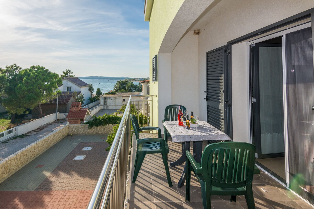 A balcony with a table and chairs, overlooking a body of water and buildings.