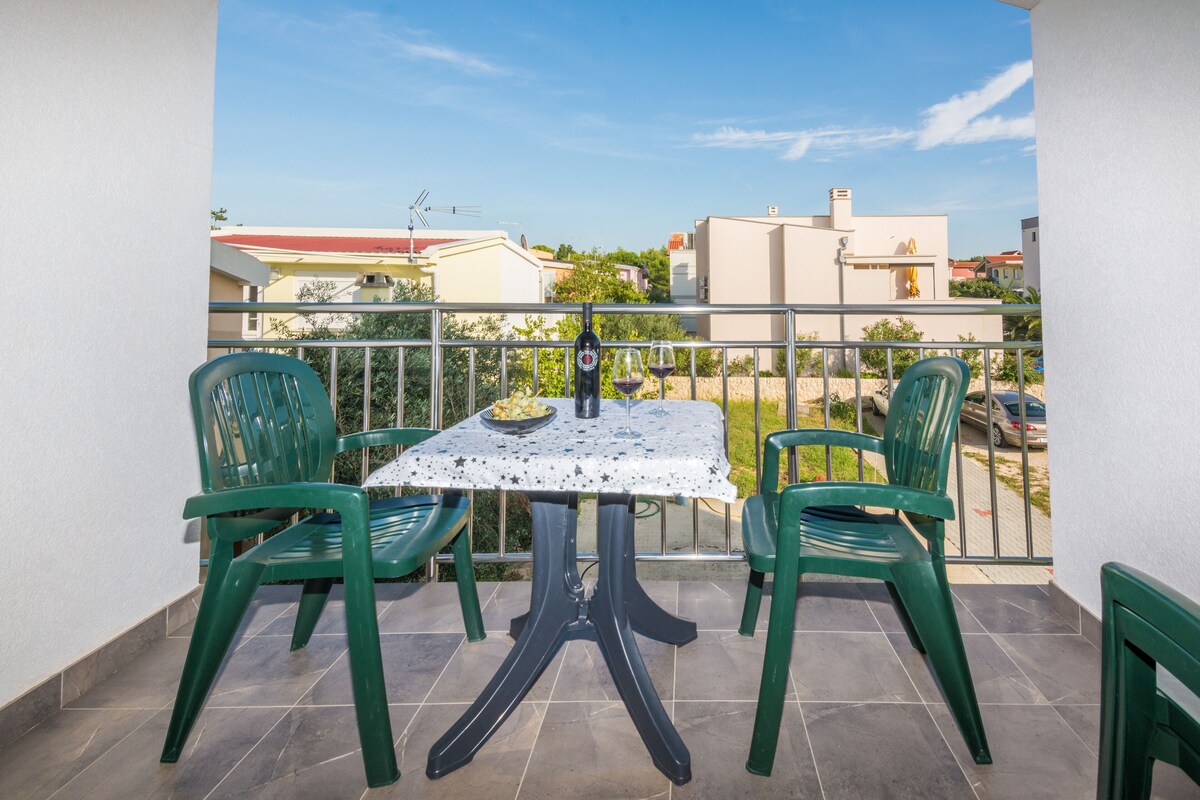 A balcony with a table and chairs, a bottle, and two glasses of wine.