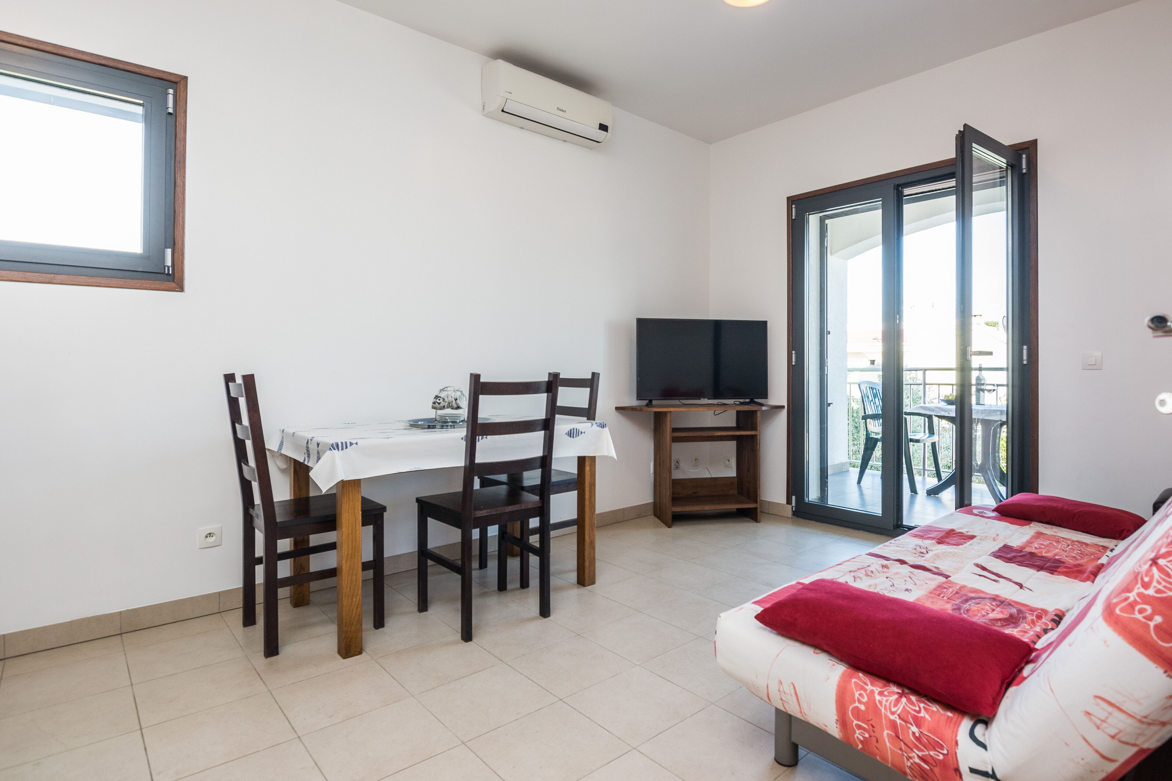A room with a bed, a dining table with chairs, a TV on a stand, and a sliding glass door leading to an outdoor area.