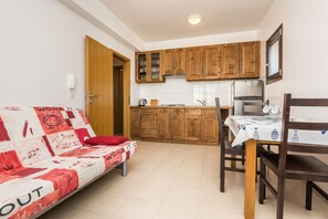 A compact kitchen with wooden cabinets, a dining table with chairs, and a sofa with a red cushion. - Apartments Silverstar (Vir)