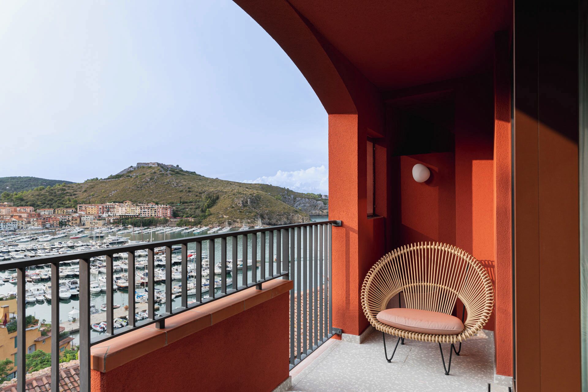 A balcony with a wicker chair, a view of a marina, and buildings in the background.