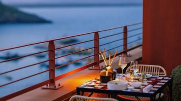 A dining table set for two with a view of the sea, a red railing, and a checkered tablecloth.