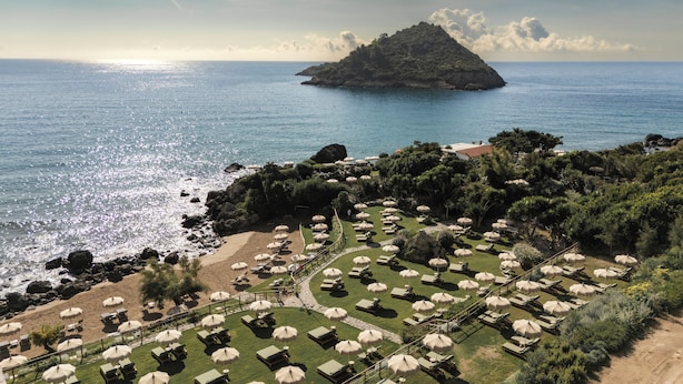 Un resort con tumbonas y sombrillas dispuestas sobre un césped, con vistas a una playa y al mar.