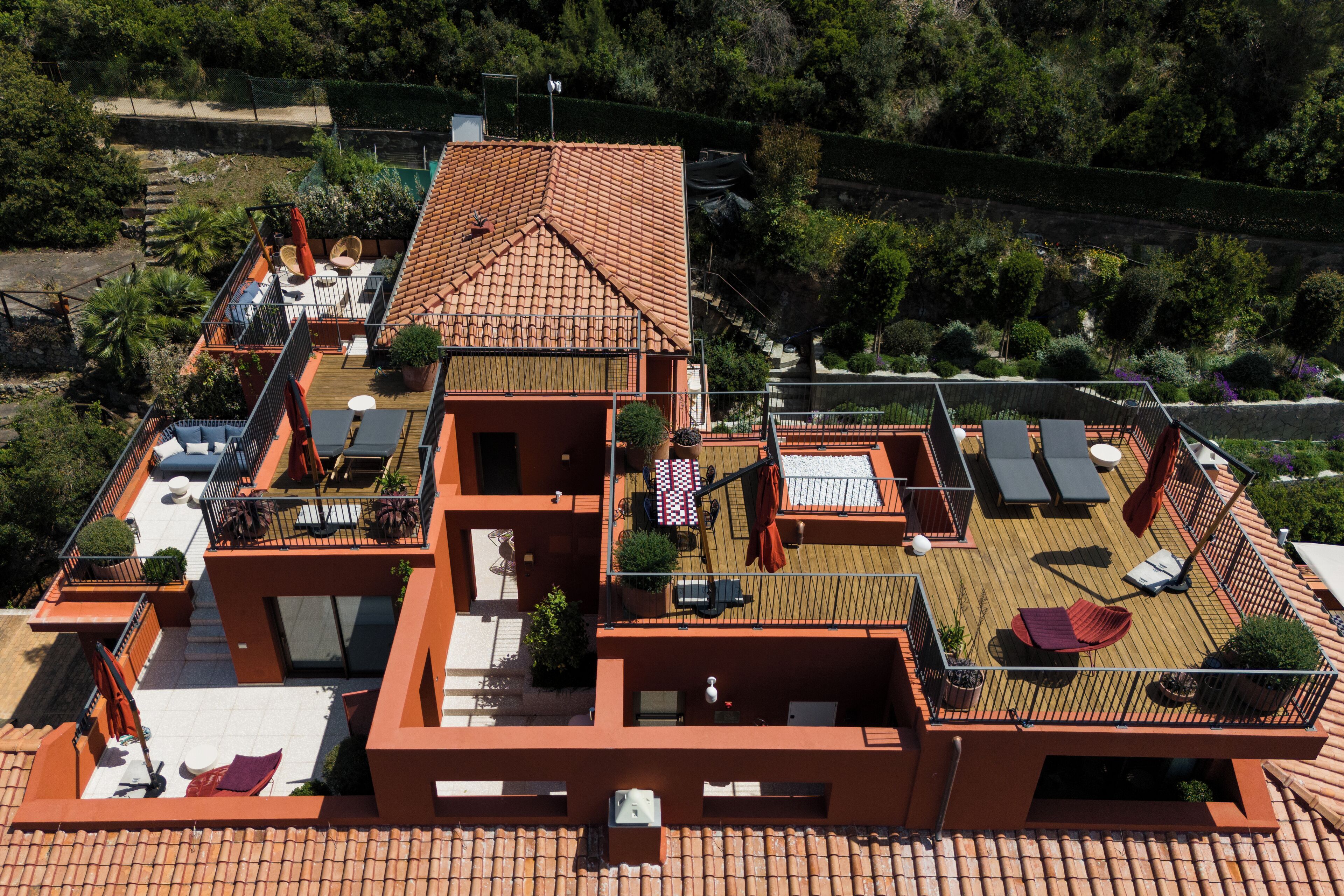A modern two-story house with a tiled roof, multiple balconies, outdoor seating areas, and a flag.