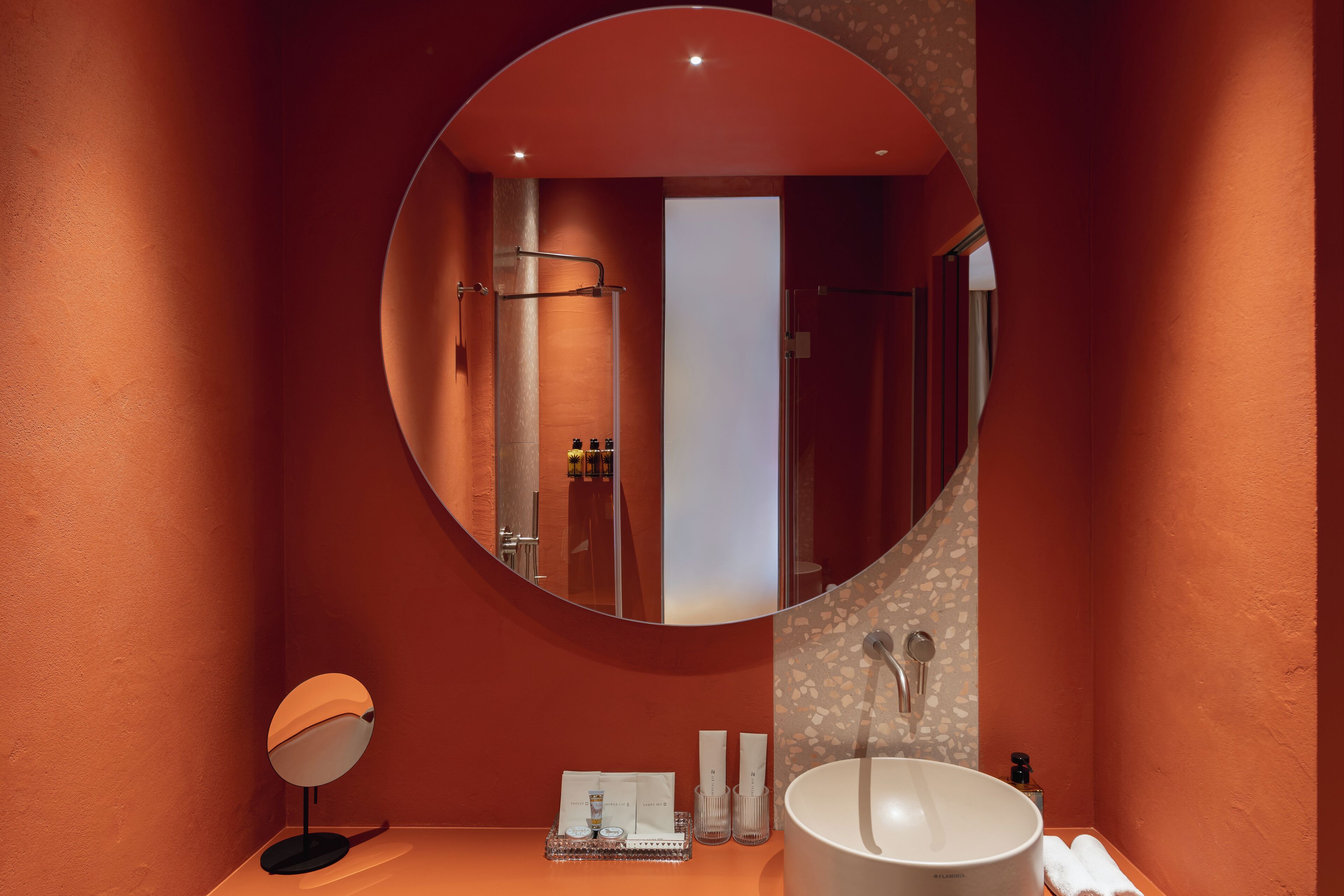 Une salle de bain avec un miroir rond, un lavabo et un espace douche.