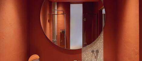 Une salle de bain avec un miroir rond, un lavabo et un espace douche.
