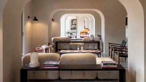 Una sala de estar moderna con sofá, reposapiés y mesa de centro, que incluye libros y una lámpara.