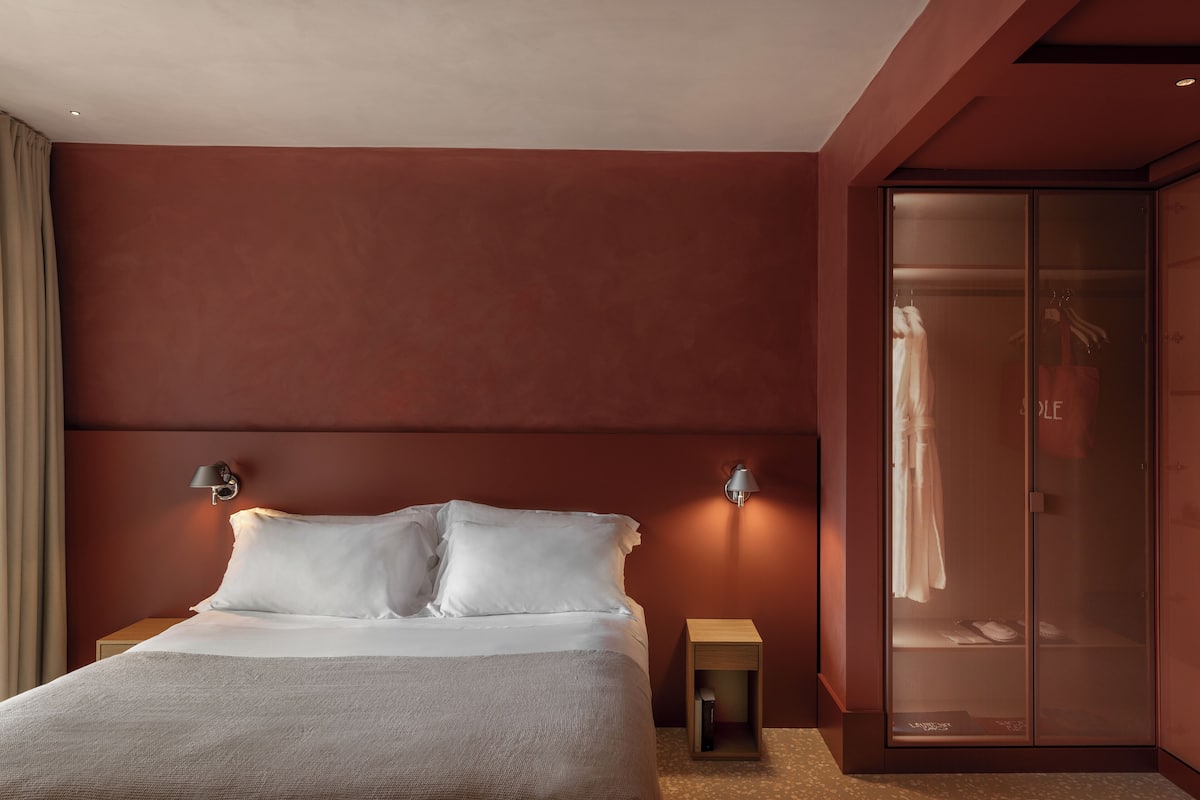 A modern bedroom with a large bed, two wall-mounted lamps, a wardrobe, and a small bedside table.