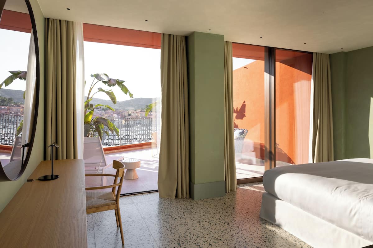 A hotel room with a bed, a desk, a chair, and a large window with curtains.