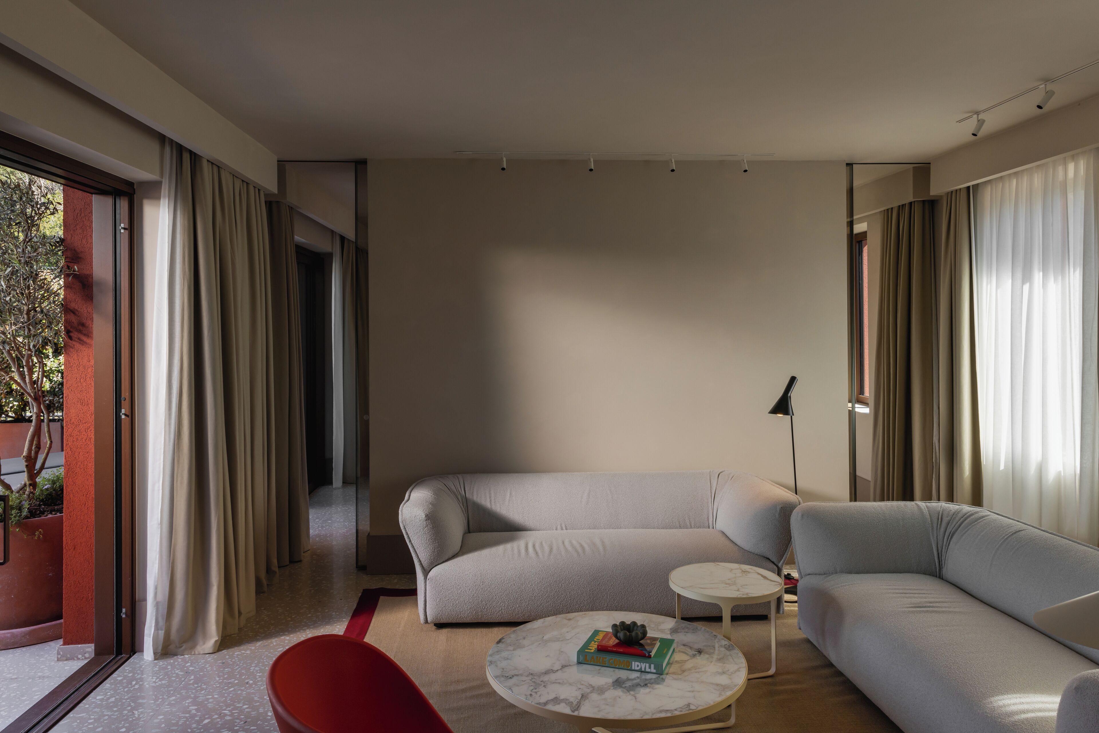 A modern living room with a light grey sofa, a round coffee table with a book, and a red chair.