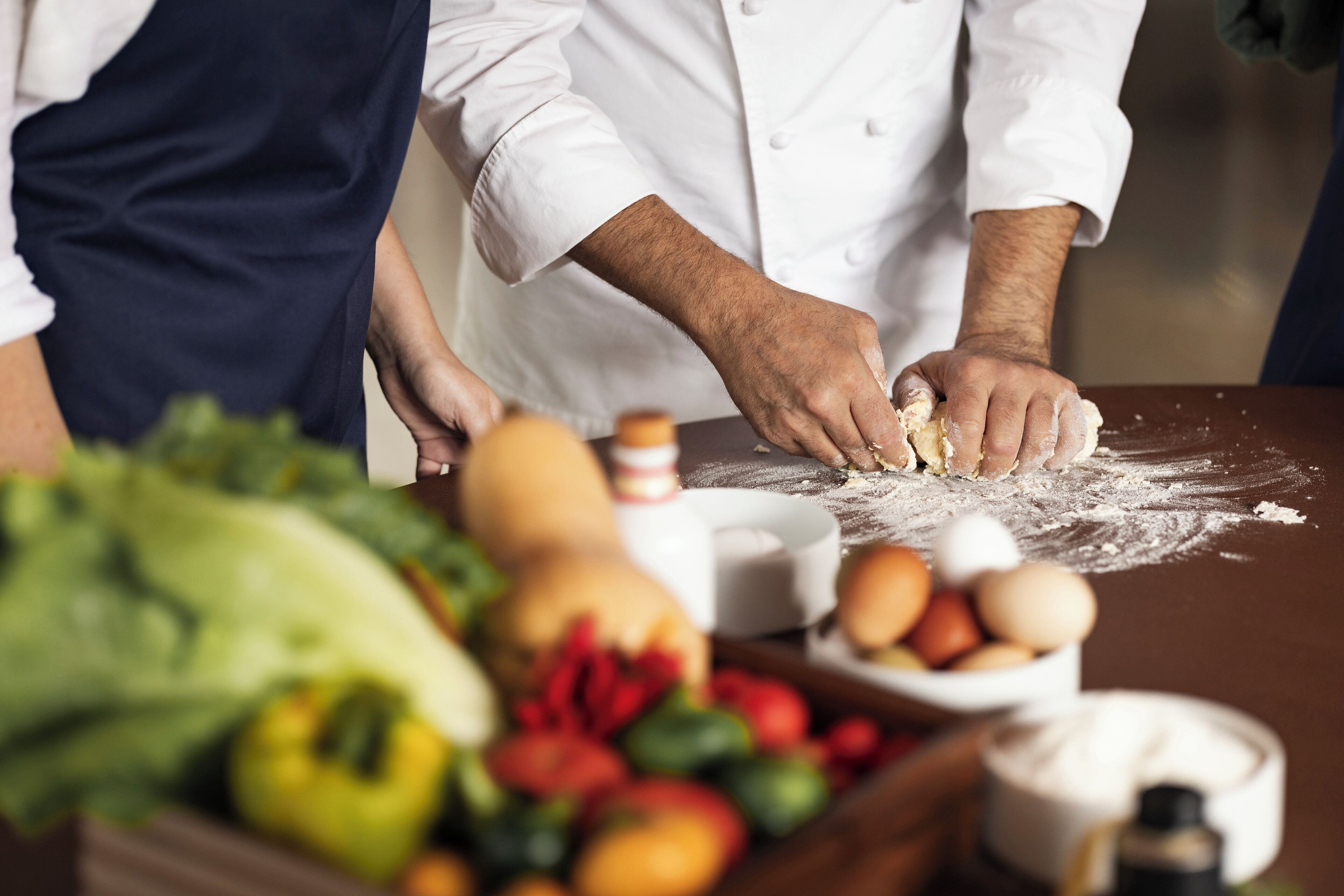 A chef preparing dough with ingredients like eggs and vegetables on a table.