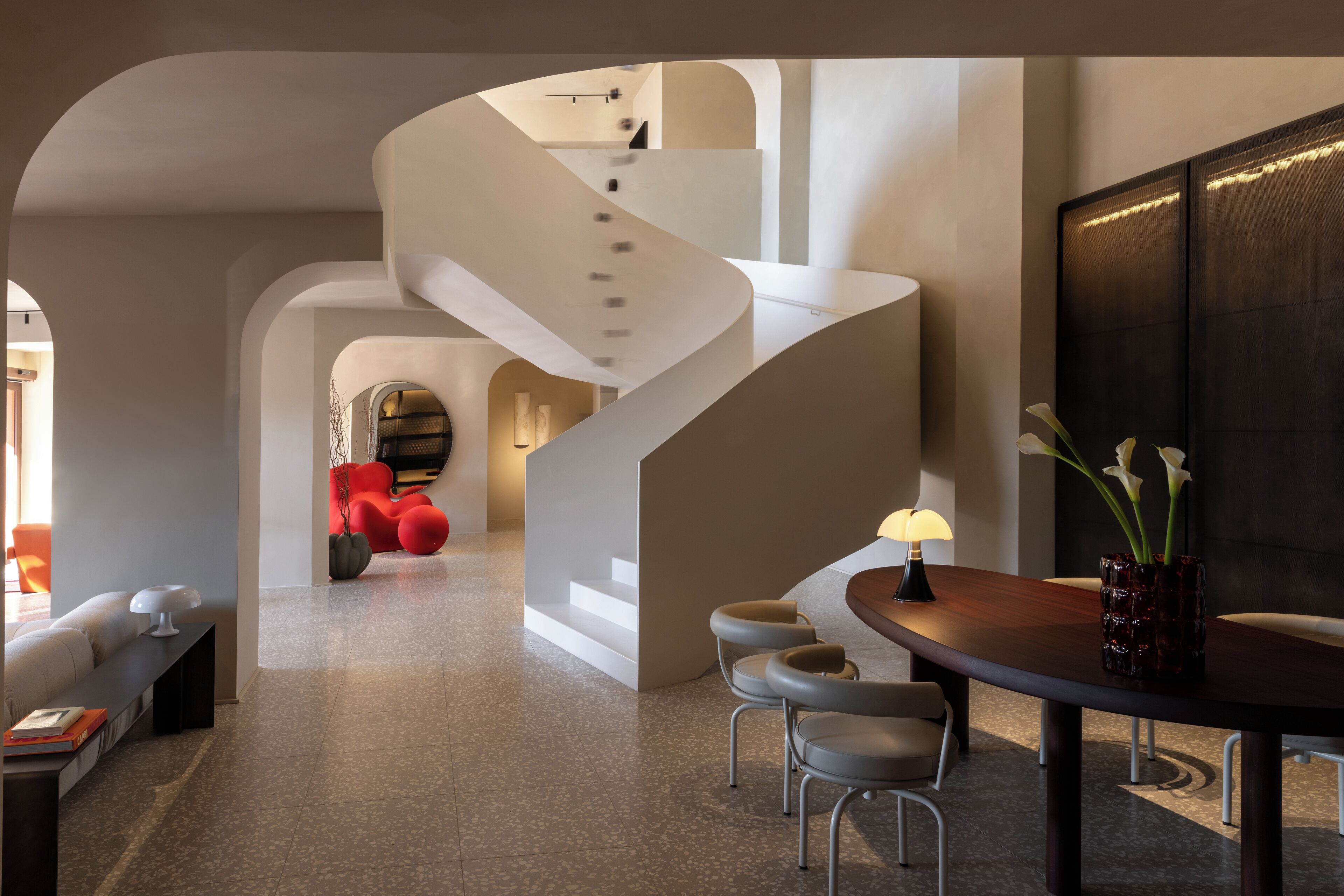 A modern interior with a spiral staircase, a dining area with a table and chairs, and a seating area with sofas.