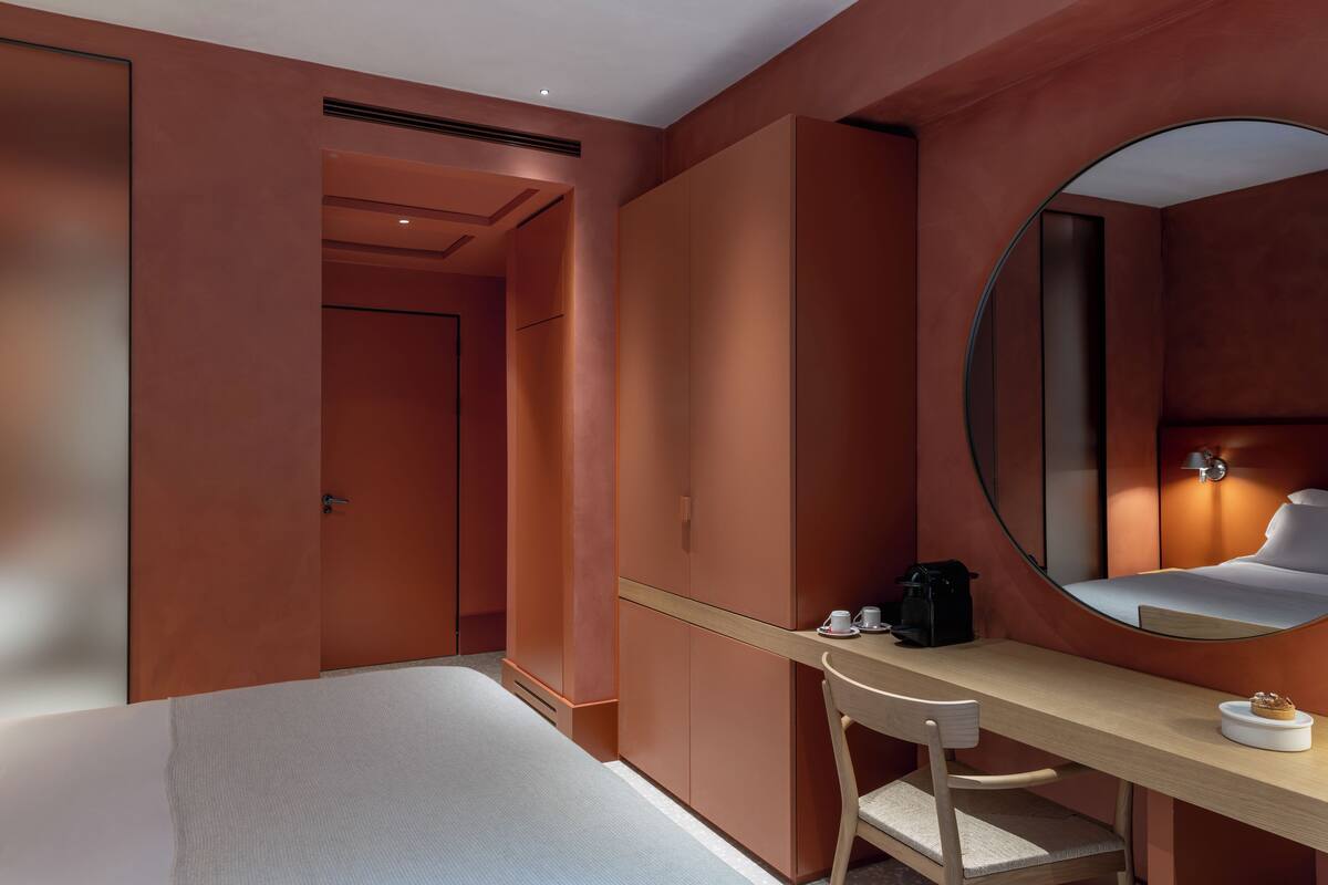 A modern hotel room with a large bed, a wooden desk, a round mirror, and built-in wardrobes.