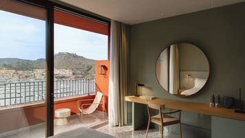 A modern hotel room with a balcony, a round mirror, a wooden desk, and a bed.