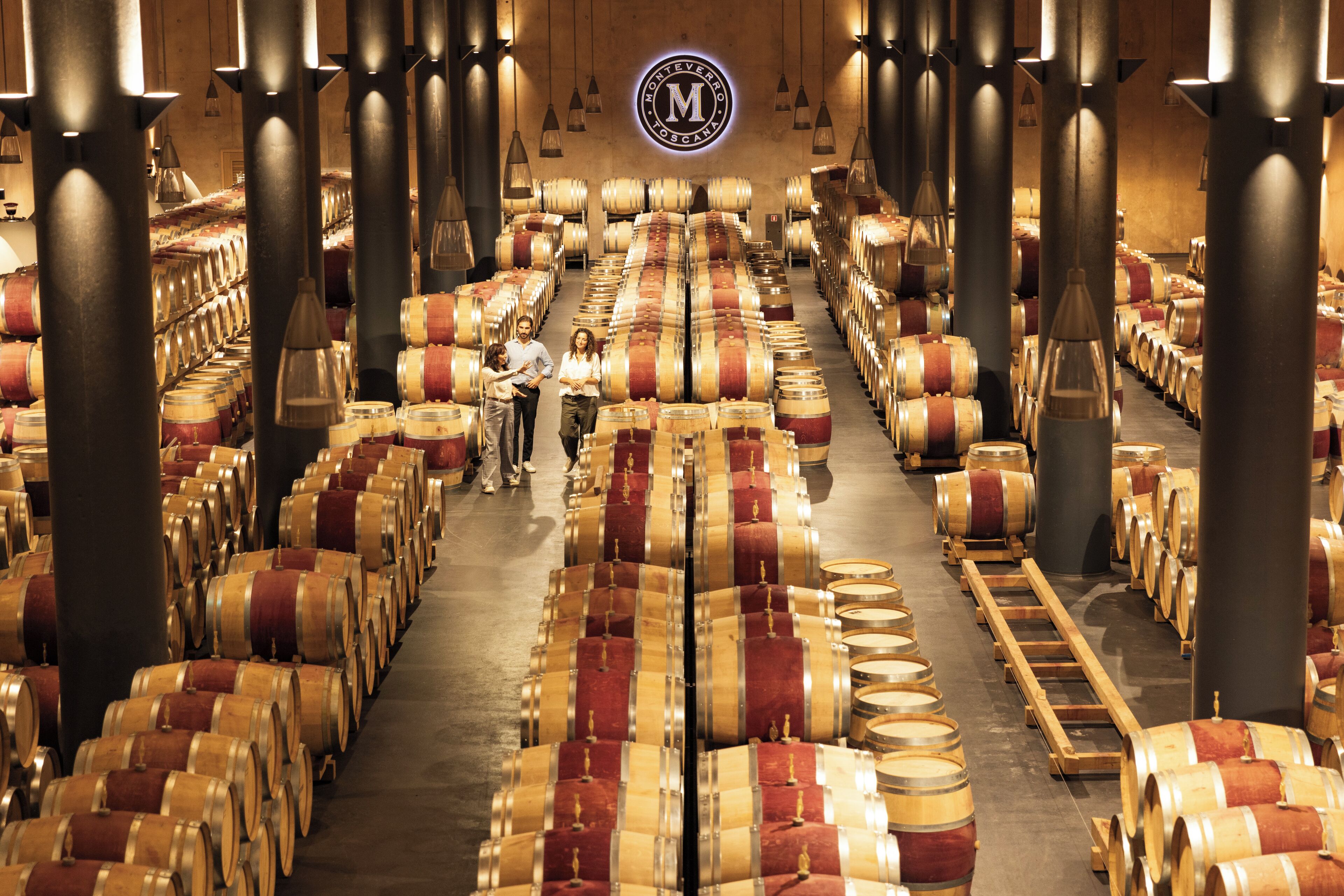 A large wine cellar with rows of wooden barrels and a central walkway.