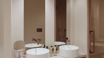 Une salle de bain moderne avec deux grands lavabos blancs, un miroir rond et une porte en bois.