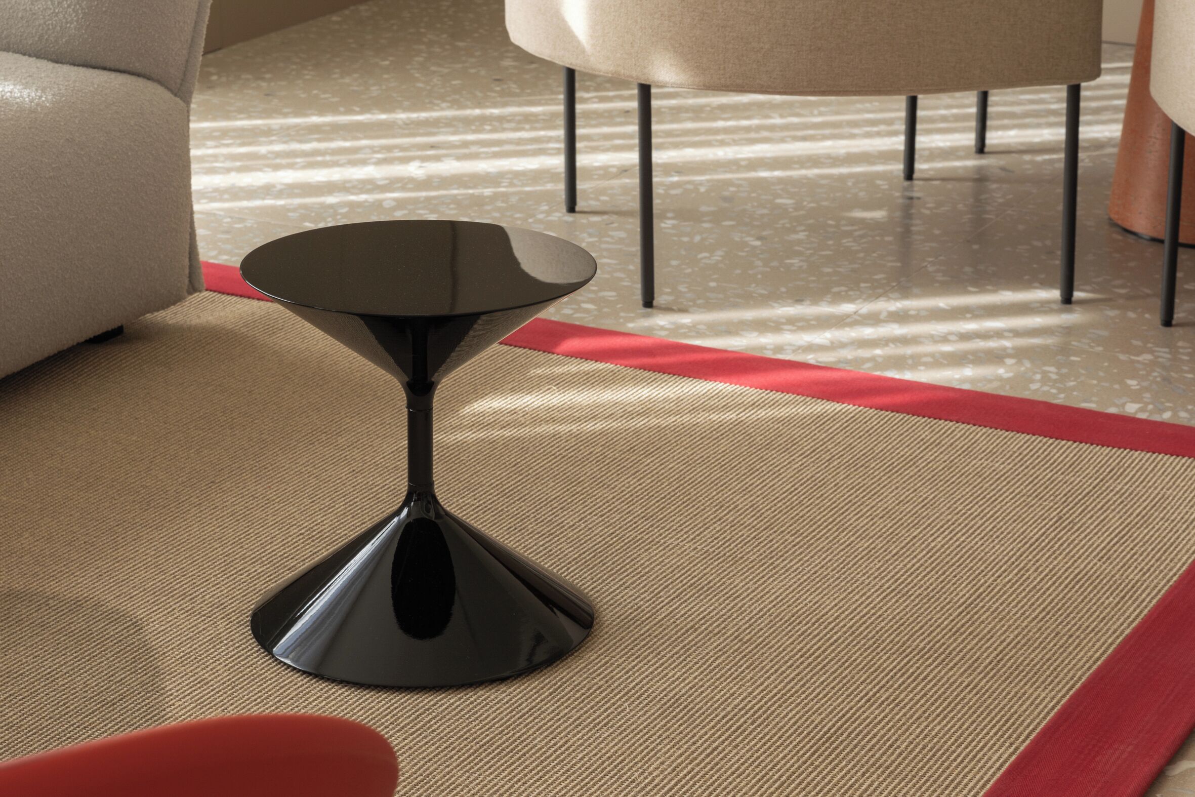 A modern living room with a black coffee table, a beige sofa, and a red accent rug.