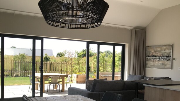 Een moderne keuken met een houten kookeiland, een eethoek met een grote tafel en stoelen, en uitzicht op een tuin door grote ramen.