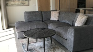 Een moderne woonkamer met een grijze modulaire bank, een klein rond bijzettafeltje en een kamerkleed met een patroon.