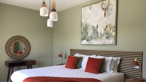 Een netjes ingerichte slaapkamer met een groot bed, een ronde spiegel, een nachtkastje en een wandlamp.