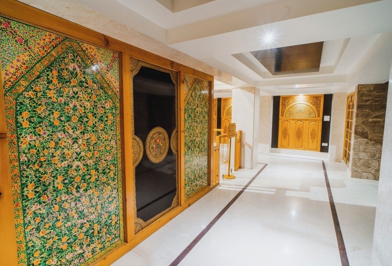 A corridor with ornate floral patterns on the walls, a wooden door with intricate designs, and a marble floor.