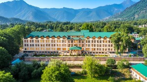 A large, multi-story hotel with a green roof, surrounded by lush greenery and mountains in the background. - Hotel The Dewan (Srinagar)