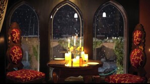 A dining table with candles and a view of a snowy landscape through arched windows. - Hotel The Dewan (Srinagar)