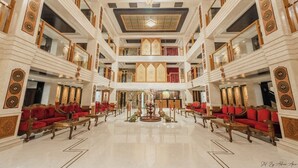 A grand lobby with multiple seating areas, a central decorative piece, and a high ceiling with intricate designs. - Hotel The Dewan (Srinagar)