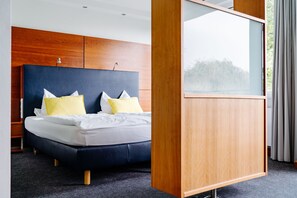 Ein modernes Hotelzimmer mit einem großen Bett, einem Holzkopfstück und Blick auf Bäume durch ein Fenster.