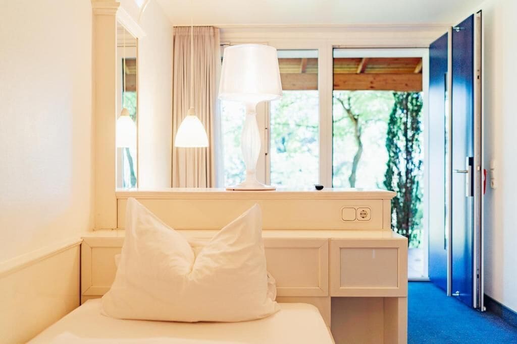 Un dormitorio con cama, escritorio, lámpara y ventana con cortinas.