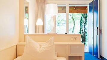 Un dormitorio con cama, escritorio, lámpara y ventana con cortinas.
