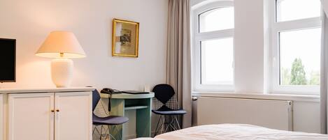 A hotel room with a bed, a desk with a chair, a lamp, a television, and a window with curtains.