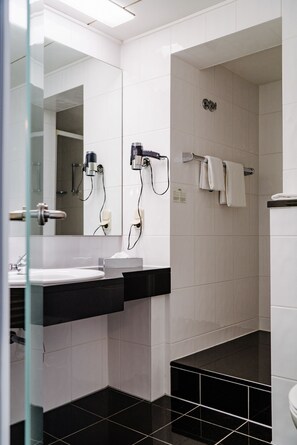 Ein modernes Badezimmer mit einem schwarz-weißen Fliesenboden, einer Glasdusche und einem weißen Waschbecken mit schwarzer Arbeitsplatte.