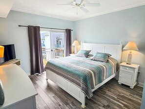 A bedroom with a bed, two bedside tables, a television, a ceiling fan, and a view of the outside balcony. - 2 Bedroom Condo with Outdoor Rooftop Pool - Midtown Ocean City! Prime location 1.5 blocks to the beach and ocean! Close to the best restuarants and bars in town! Sunset Bay 418 (Ocean City)