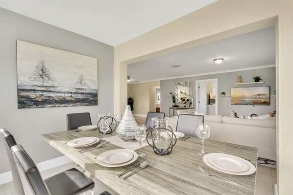 A dining area with a long table set for six, a modern kitchen in the background, and a living area with a sofa and a TV. - RiversideStar: Pompano Retreat, close to beach (Pompano Beach)