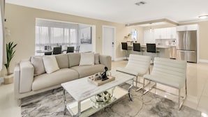 A modern living room with a sofa, a coffee table, and a dining area with chairs. - RiversideStar: Pompano Retreat, close to beach (Pompano Beach)