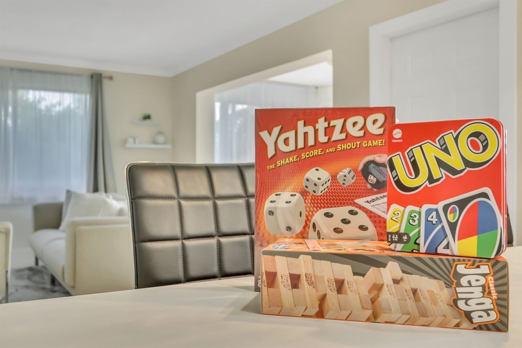 Eine Yahtzee UNO Spielbox auf einem Tisch in einem Raum mit einem grau gepolsterten Sessel und einem weißen Sofa.