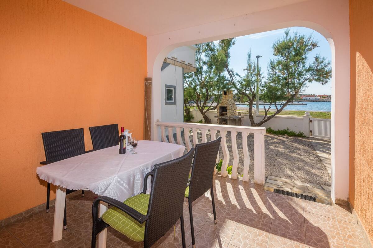 Un patio con mesa y sillas, un horno de piedra y vistas a un cuerpo de agua y árboles.