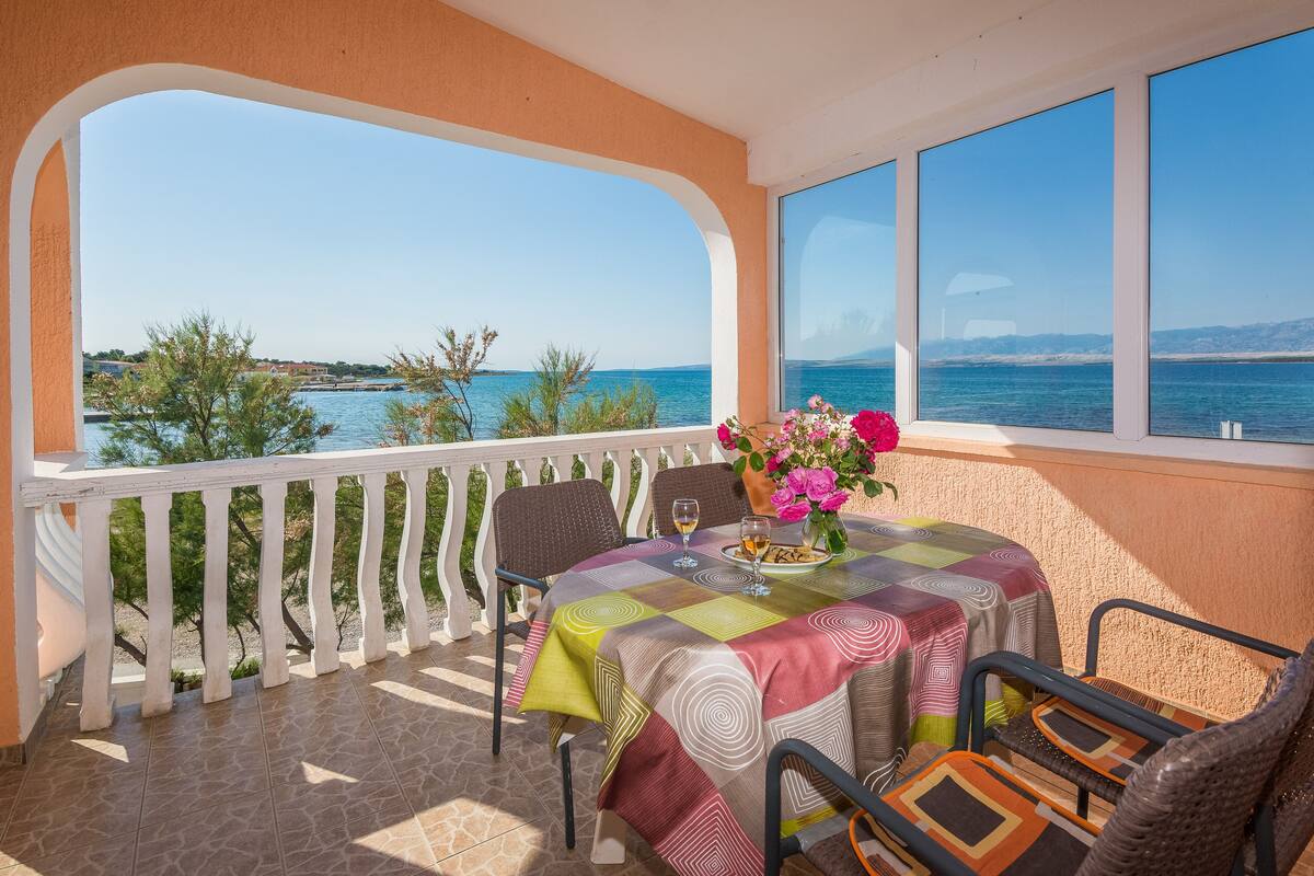 Un balcón con una mesa preparada para dos personas, con vistas a la costa.