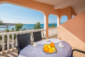 Ein Balkon mit Tisch für zwei Personen, ausgestattet mit Obstkorb, zwei Weingläsern und Blick auf das Meer und Gebäude.