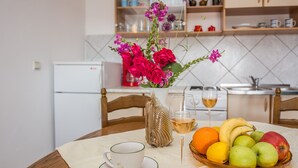 Ett matbord med en vit kopp, ett glas vitt vin, en fruktskål och en vas med blommor.