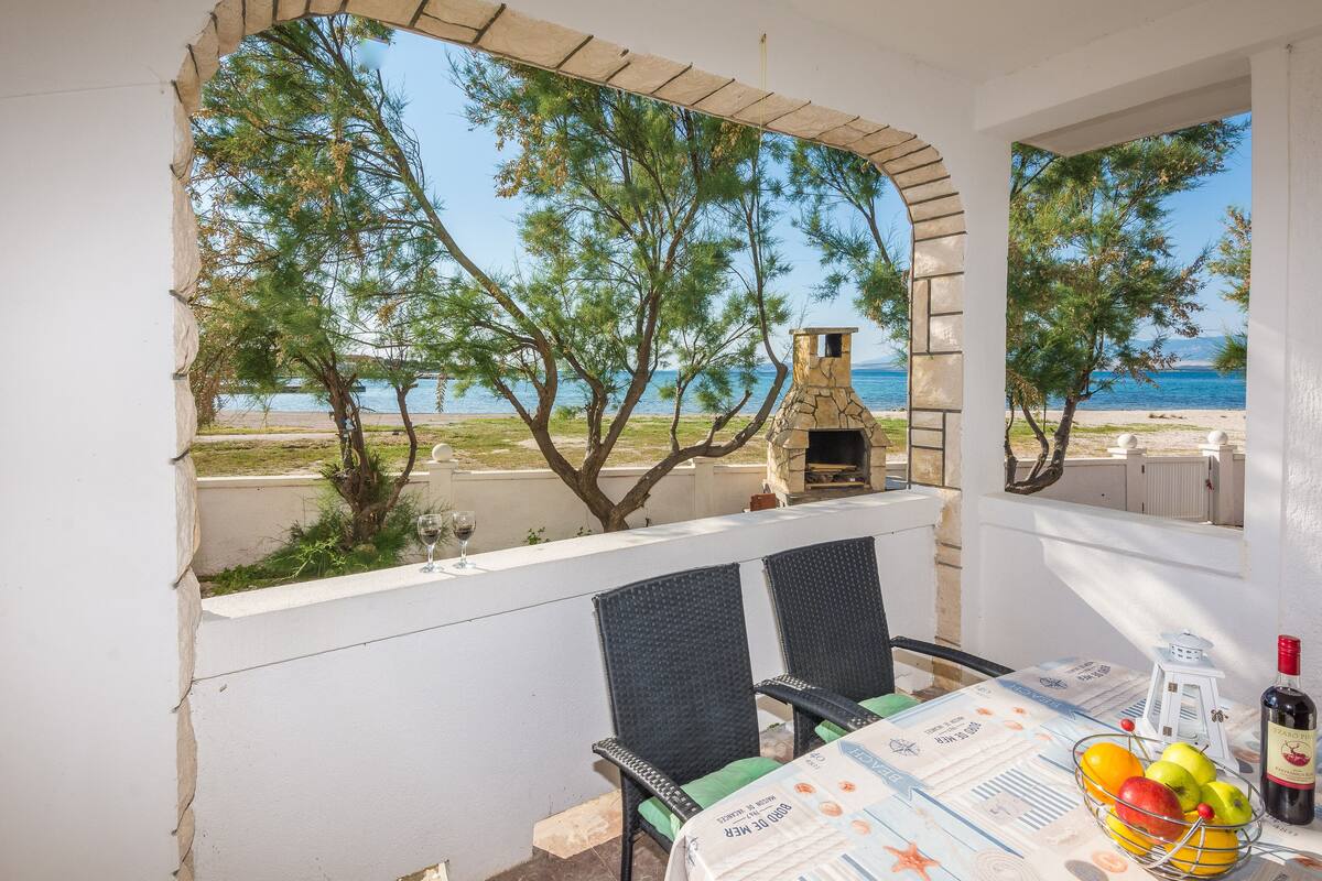 Una terraza con mesa lista para comer, vista al mar y chimenea de piedra.