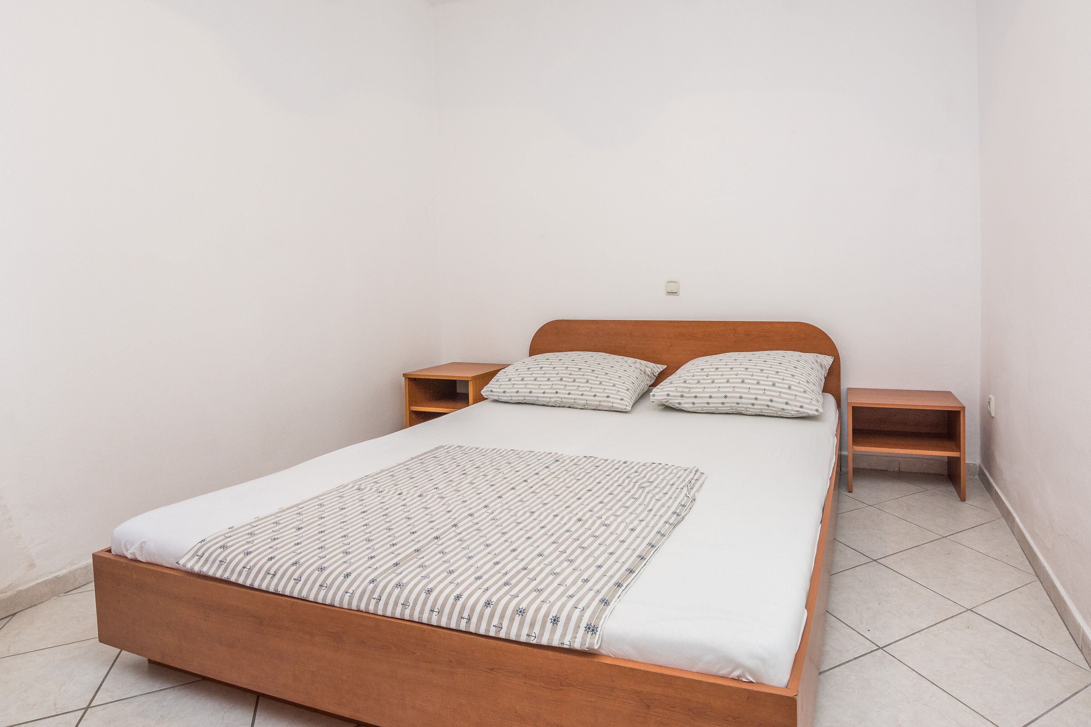Habitación individual con una cama de madera, dos mesitas de noche y una colcha estampada.