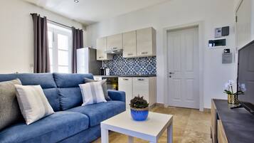 A modern living room with a blue sofa, a white coffee table, and a kitchen area with light-colored cabinets and blue patterned backsplash.