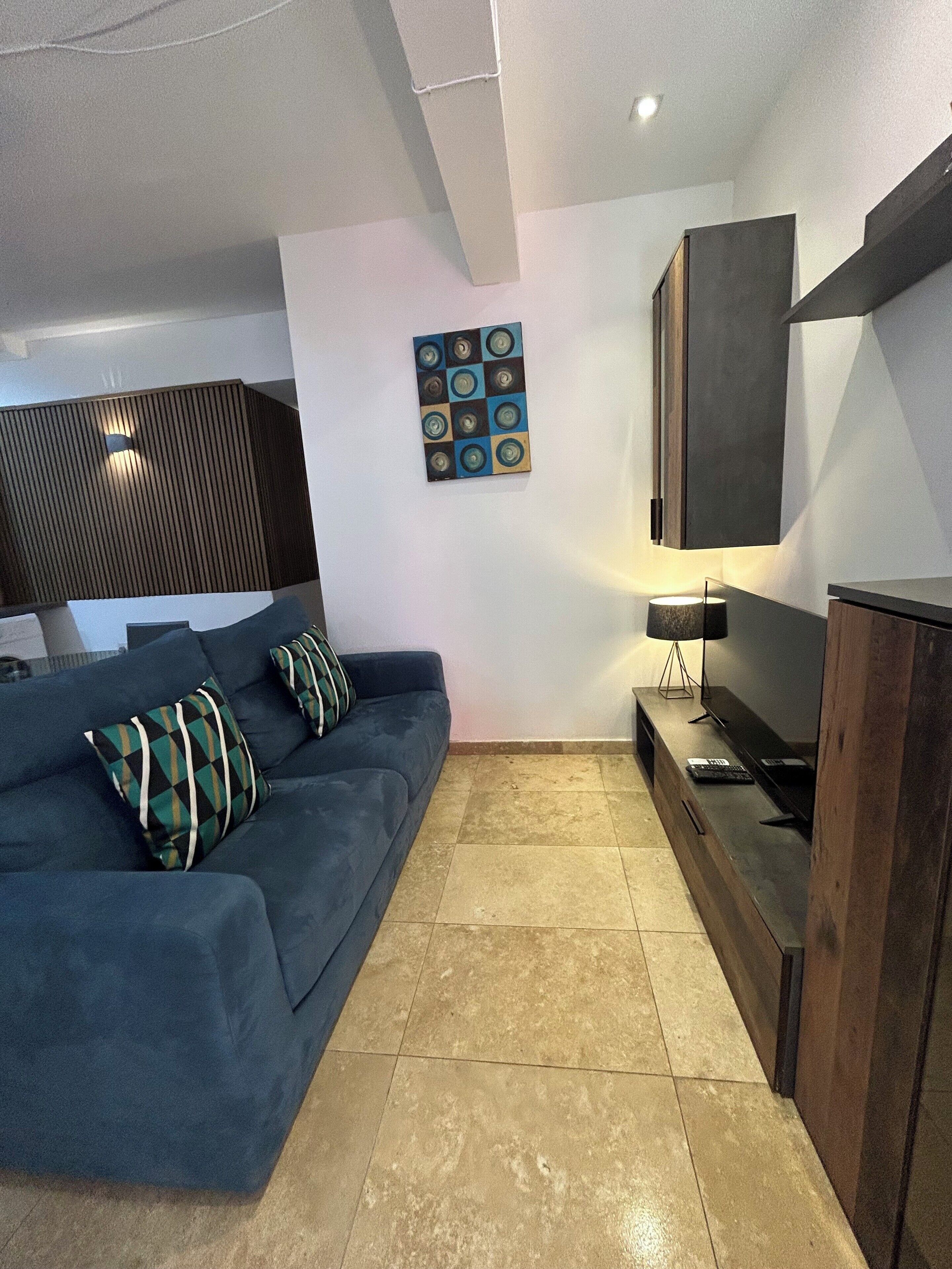 Un salon moderne avec un canapé bleu, un téléviseur à écran plat, un meuble en bois et un élément décoratif mural.