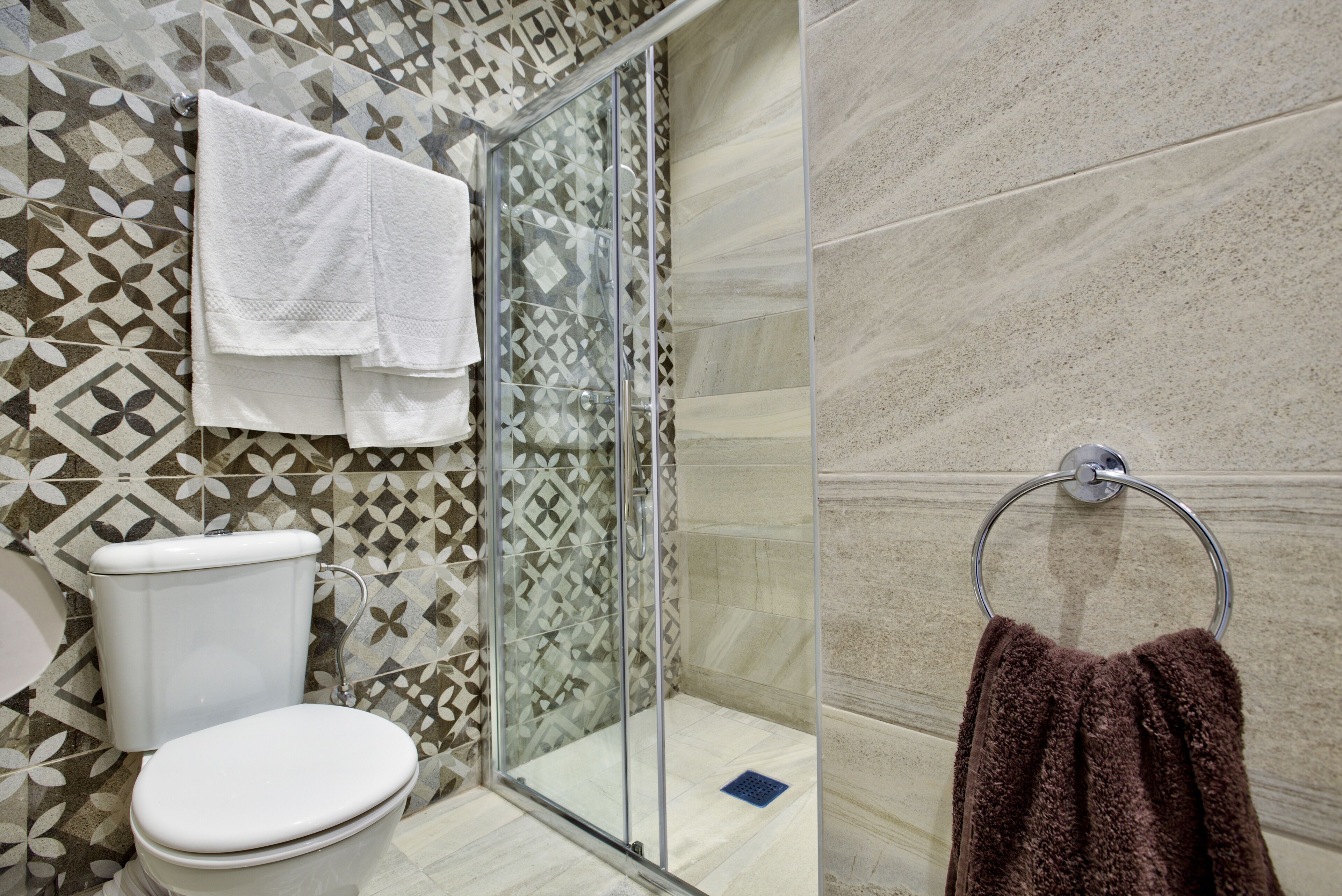 Un baño con inodoro, cabina de ducha de vidrio y toallero con toalla.