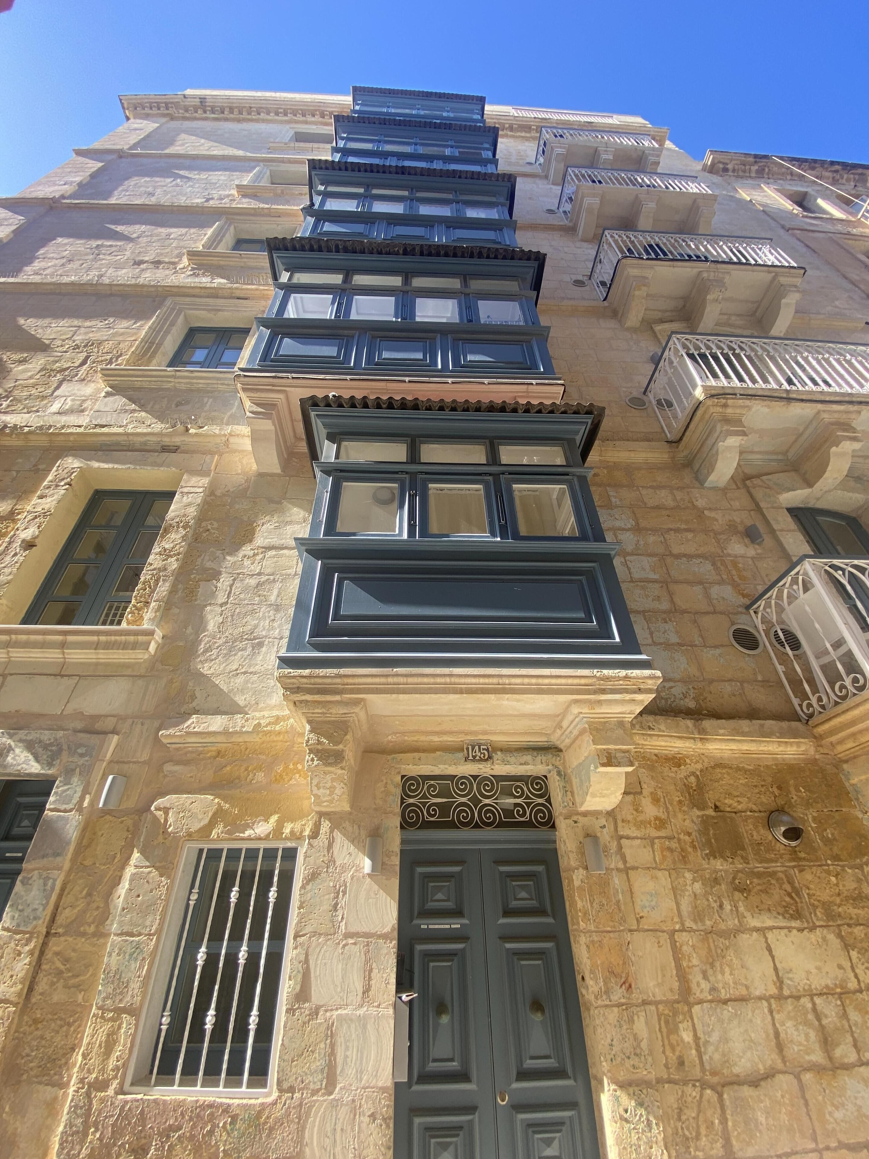 Un edificio de varios pisos con fachada de piedra, varios balcones y una entrada destacada con una reja de metal.