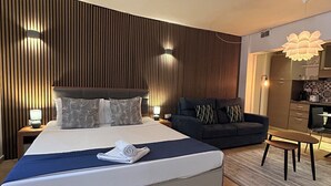 A modern hotel room with a large bed, a sofa, a small table, and a kitchen area. - Ursula Suites- Self Catering Apartments- Valletta- by Tritoni Hotels (Valletta)