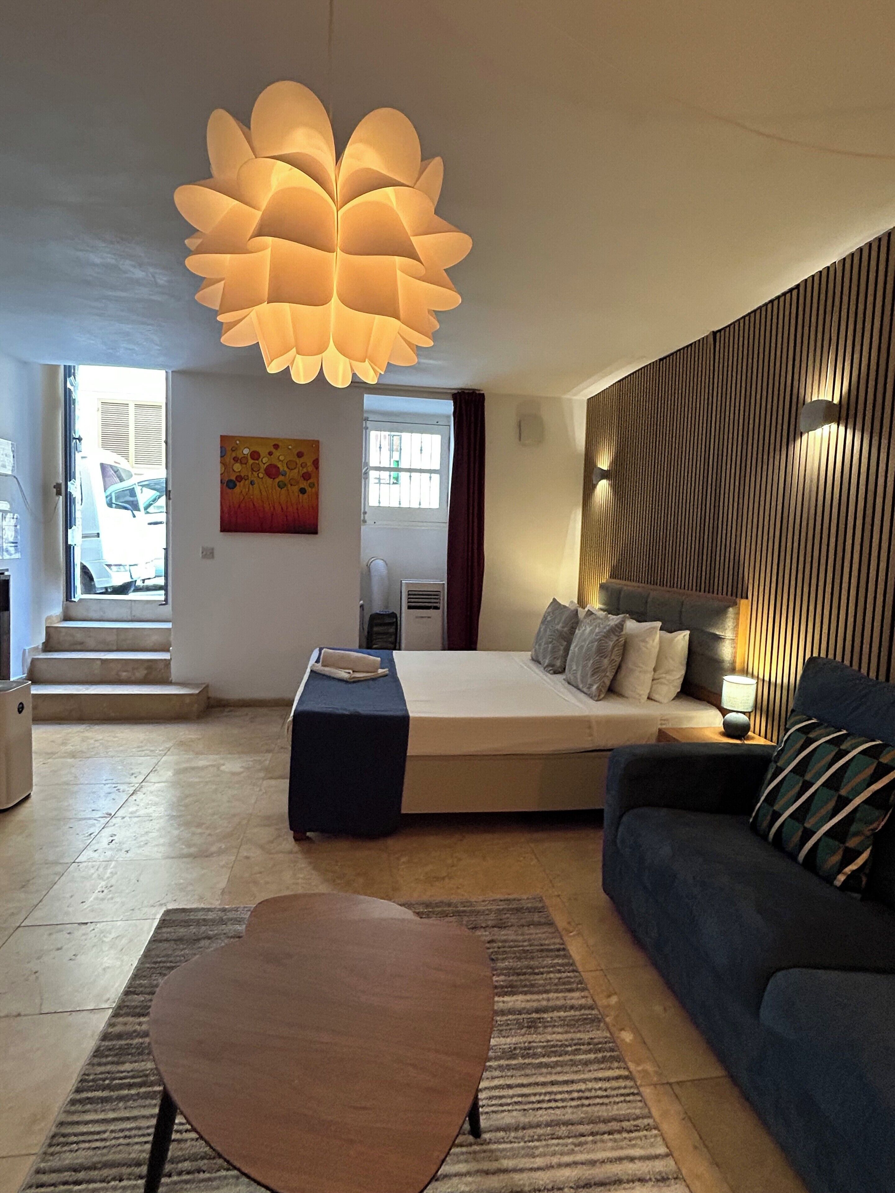 A modern hotel room with a large bed, a sofa, a coffee table, and a unique ceiling light fixture.