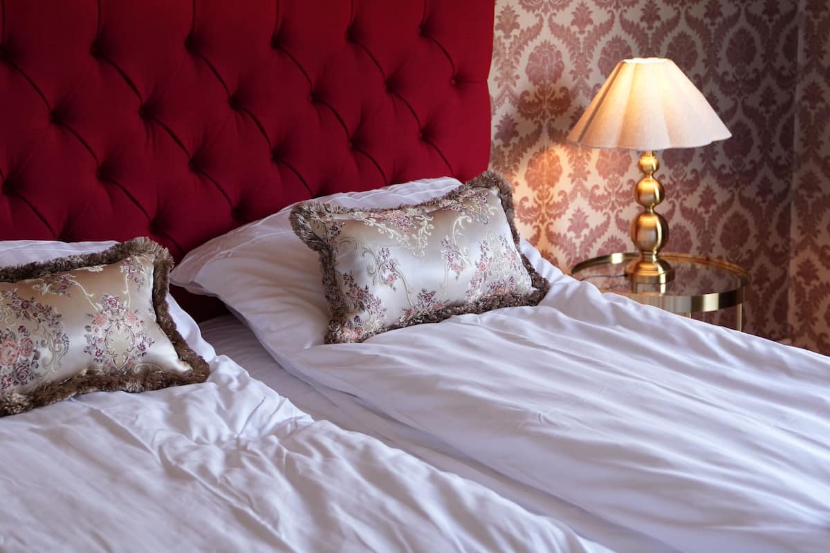 Una cama con sábanas blancas, cabecera roja y almohadones decorativos.